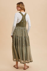 woman wearing a long olive green tiered maxi dress with floral embroidery and a white long sleeve top underneath