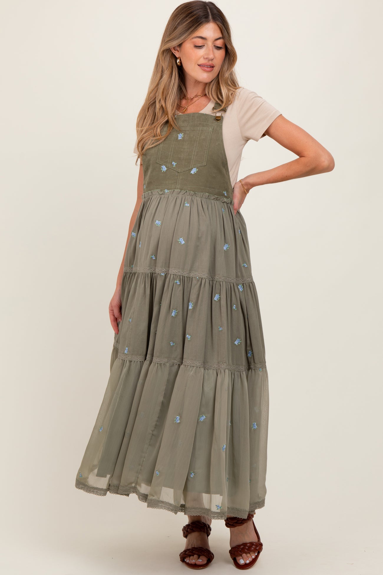 woman wearing a long olive green maternity dress with tiered design and floral embroidery over a light beige top