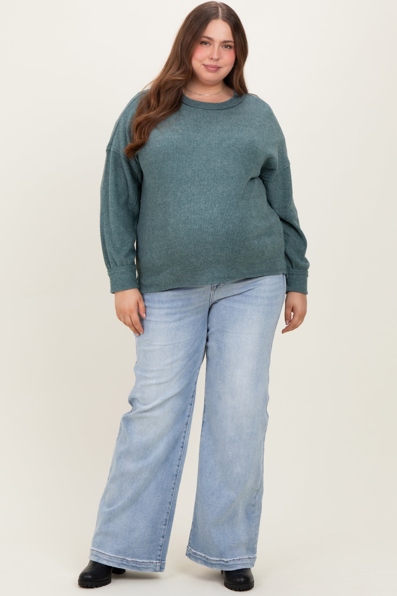woman wearing a teal oversized sweater and light blue wide-leg jeans, showcasing her baby bump