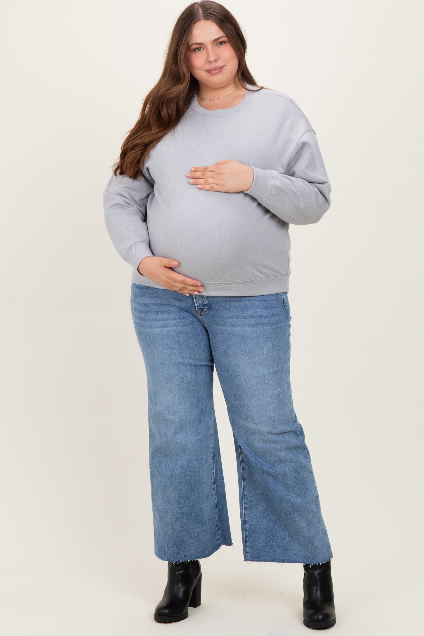woman wearing a gray maternity sweatshirt and blue flared jeans, holding her baby bump