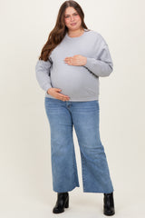 woman wearing a gray maternity sweatshirt and blue flared jeans, holding her baby bump