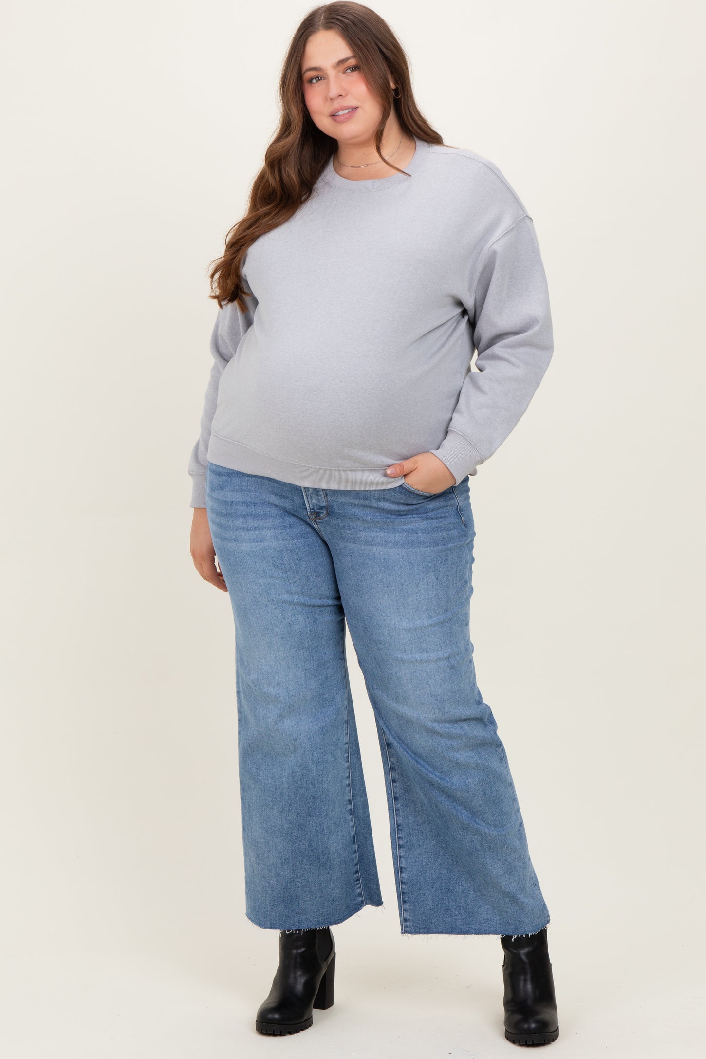 woman wearing a gray oversized sweatshirt and blue wide-leg jeans, showing her baby bump in maternity plus attire