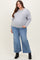 woman wearing a gray oversized sweatshirt and blue wide-leg jeans, showing her baby bump in maternity plus attire