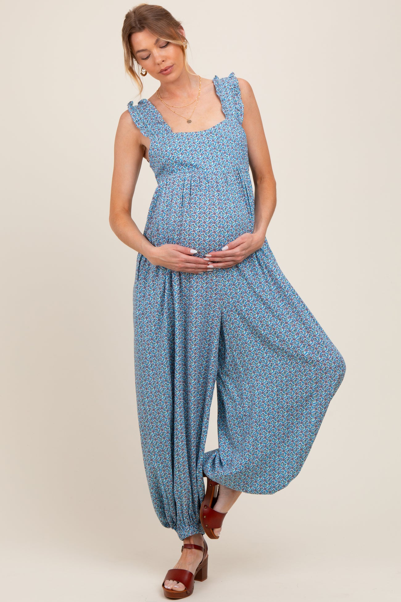woman wearing a blue floral maternity jumpsuit with ruffled straps and a visible baby bump