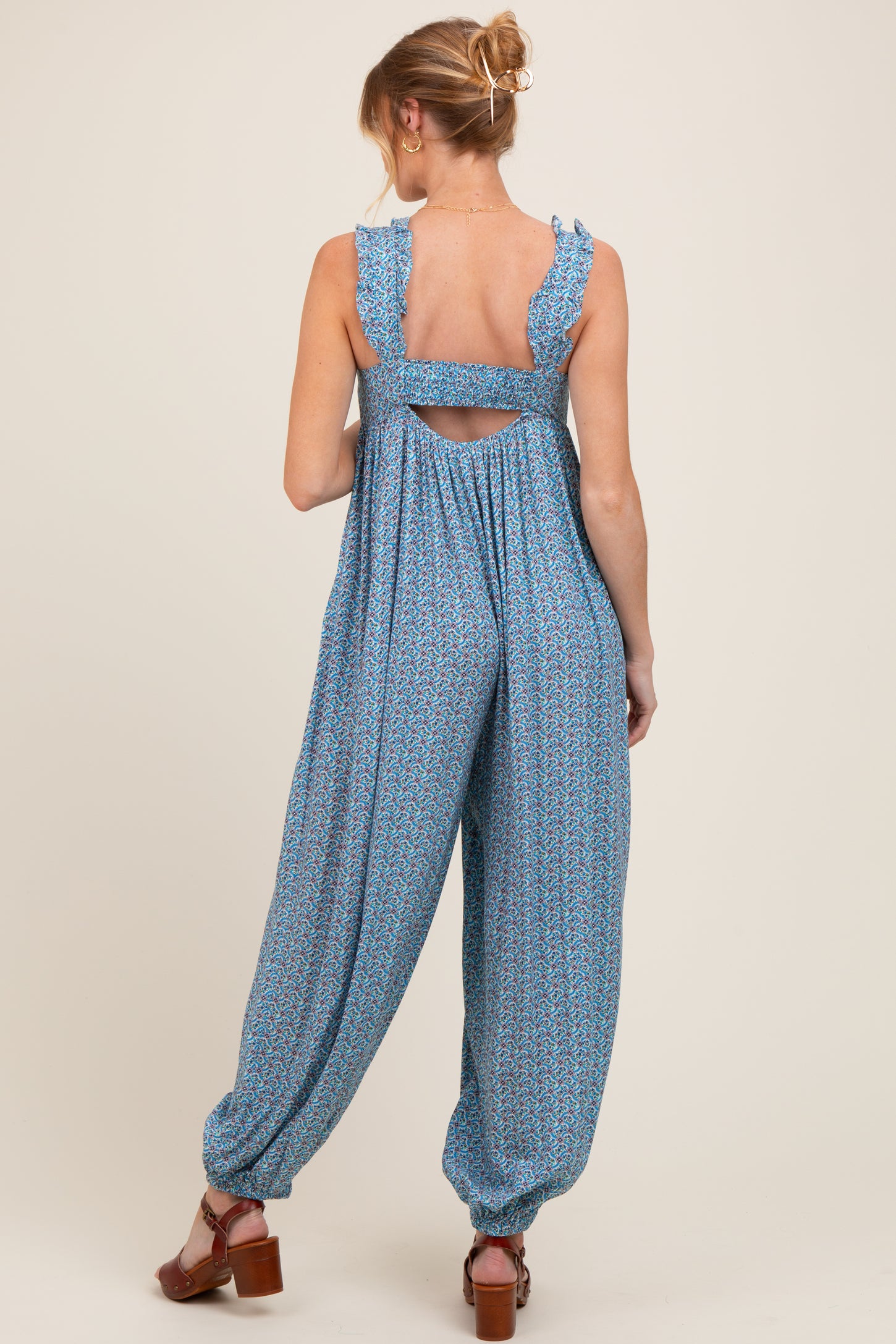 woman wearing a blue floral patterned maternity jumpsuit with ruffled straps and an open back, showcasing a baby bump