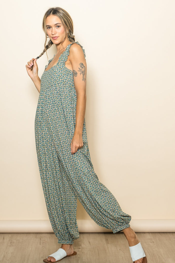 woman wearing a green floral jumpsuit with adjustable ties and loose fit, standing with braids in her hair