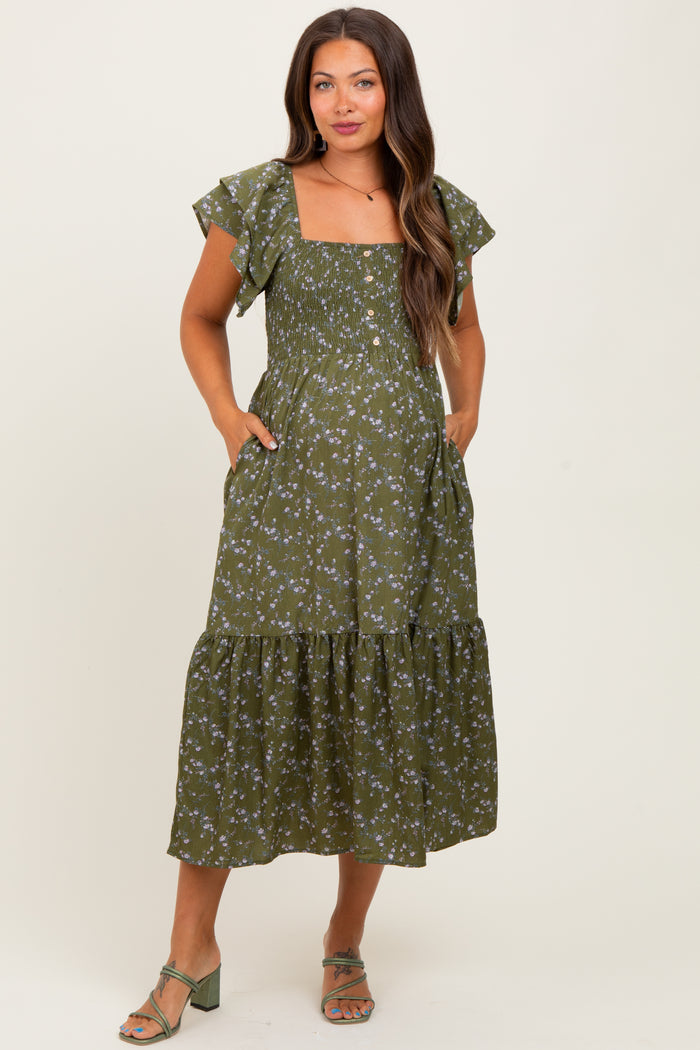 woman wearing a green floral print maternity dress with flutter sleeves and pockets, styled with sandals