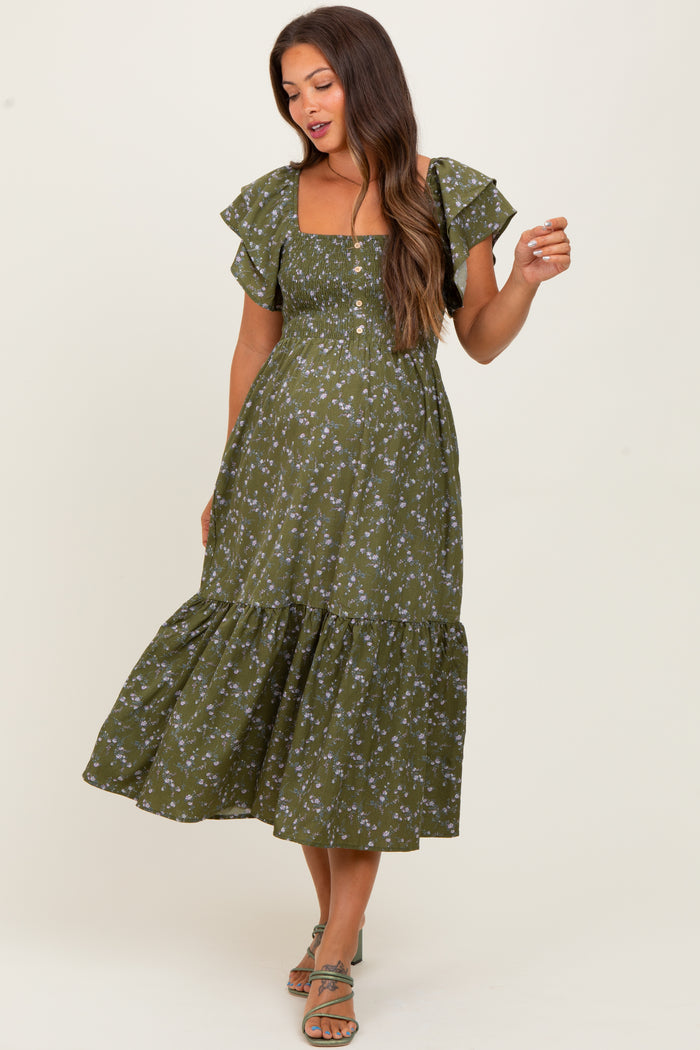 woman wearing a green floral print maternity dress with ruffled sleeves and a tiered skirt, holding one hand playfully
