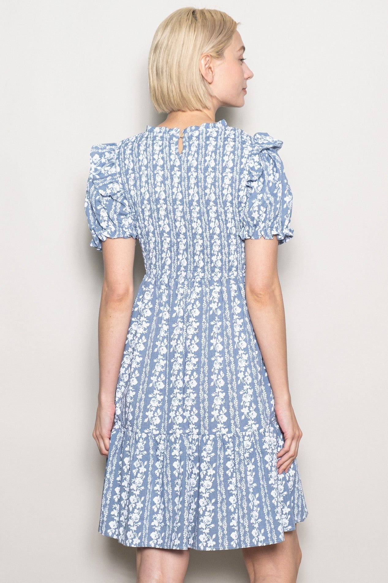 woman wearing a blue floral puff sleeve dress with a tiered skirt, viewed from the back