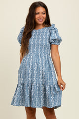 woman wearing a blue floral maternity dress with puff sleeves and a tiered skirt, smiling at the camera
