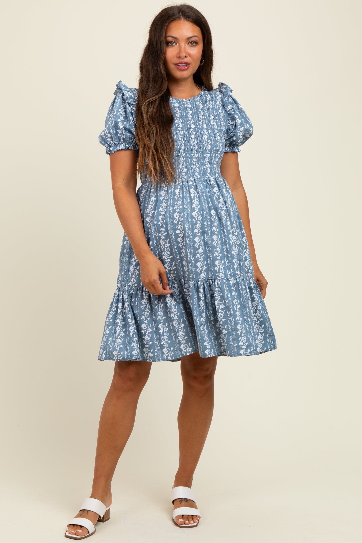 woman wearing a blue floral maternity dress with puff sleeves and a tiered skirt, showcasing her baby bump