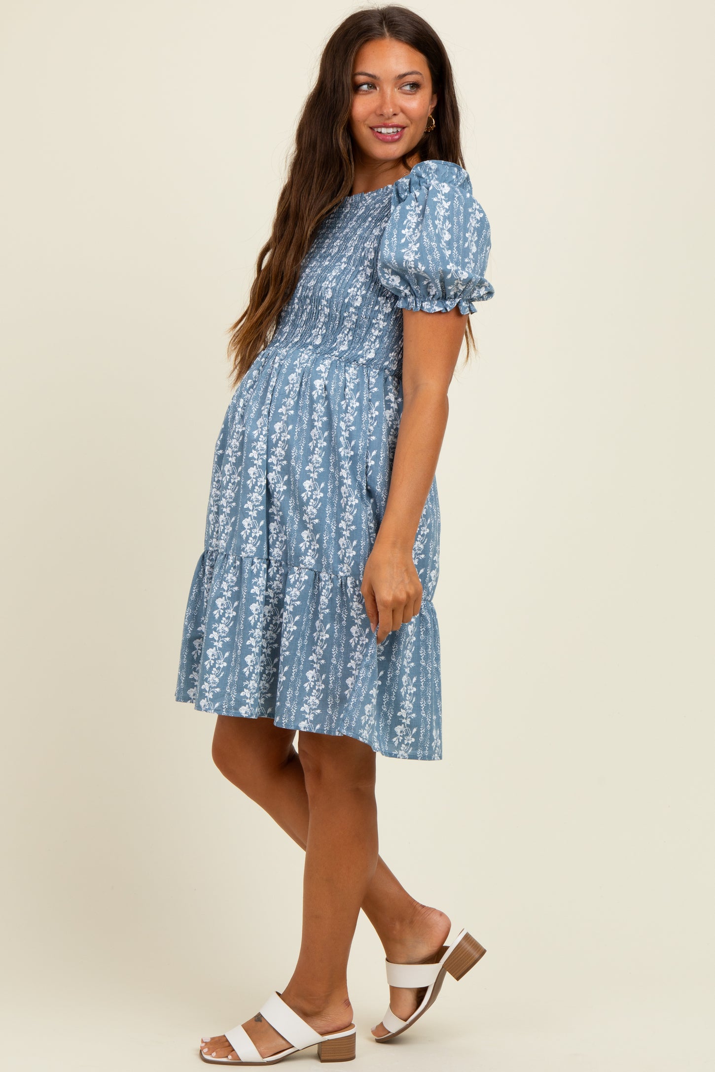 woman wearing a light blue floral print maternity dress with puff sleeves and a tiered skirt, showcasing her baby bump