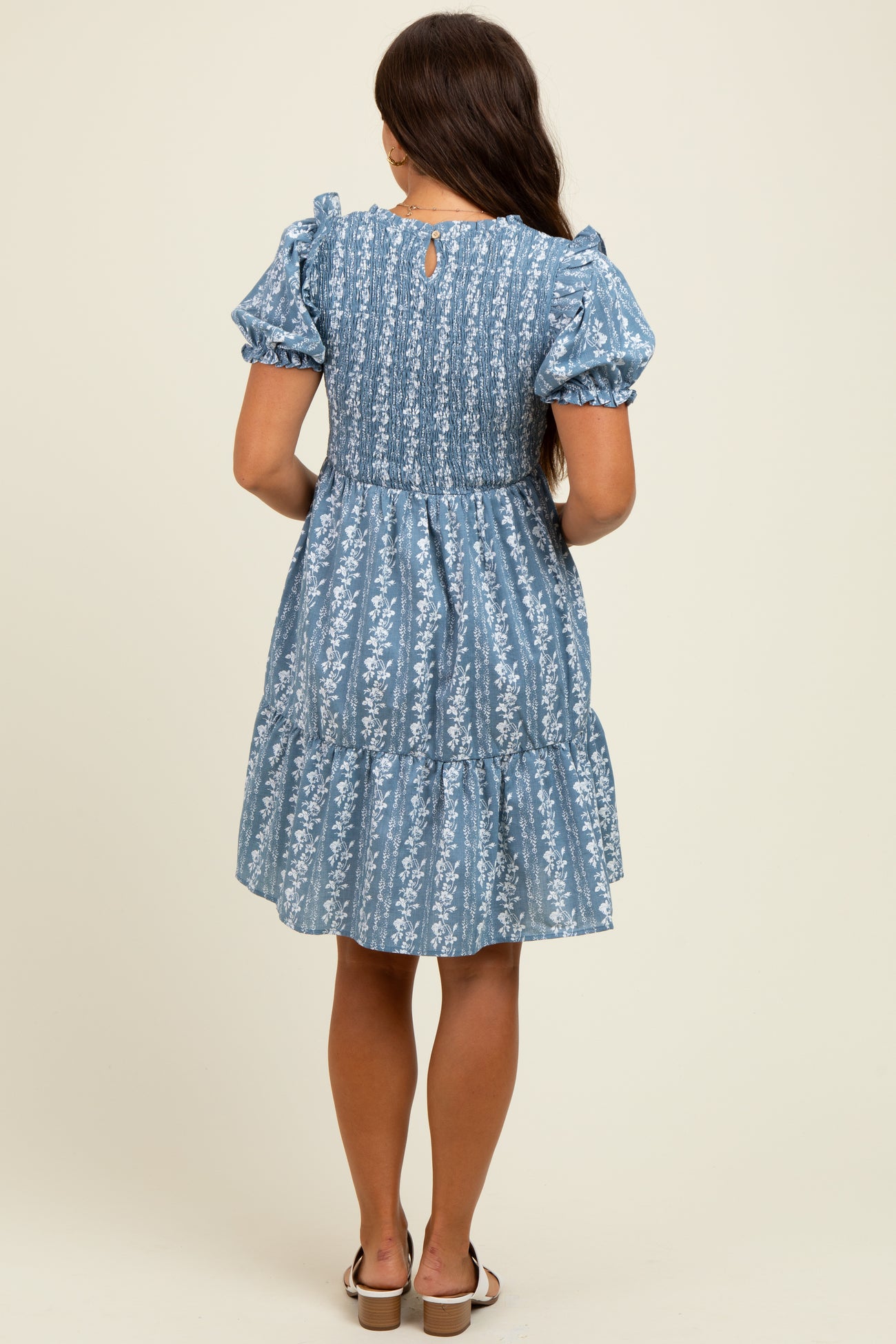 woman wearing a blue floral print maternity dress with puff sleeves and tiered skirt, showing a stylish back view