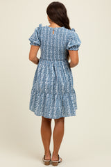 woman wearing a blue floral print maternity dress with puff sleeves and tiered skirt, showing a stylish back view