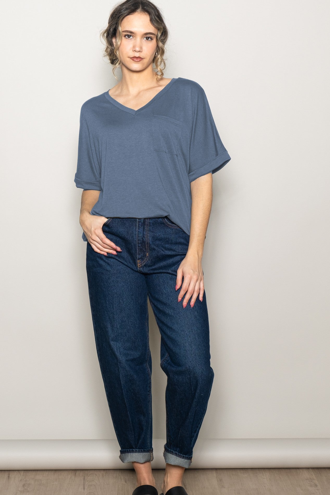 woman wearing a blue v-neck t-shirt and high-waisted jeans, standing with one hand on hip