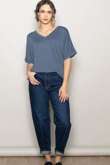 woman wearing a blue v-neck t-shirt and high-waisted jeans, standing with one hand on hip