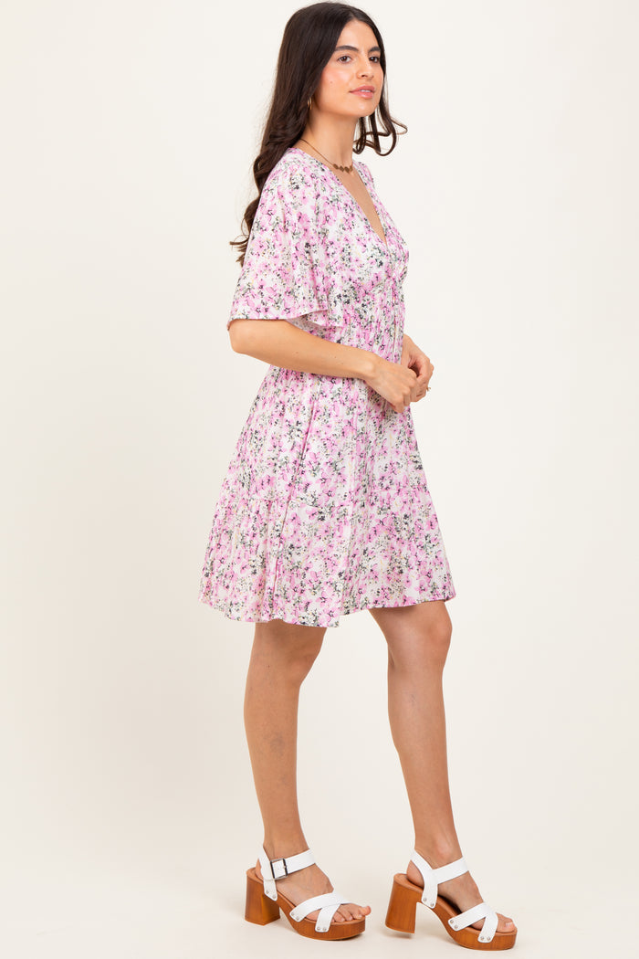 woman wearing a pink floral short sleeve dress with a v-neck and flared hem, paired with white heeled sandals