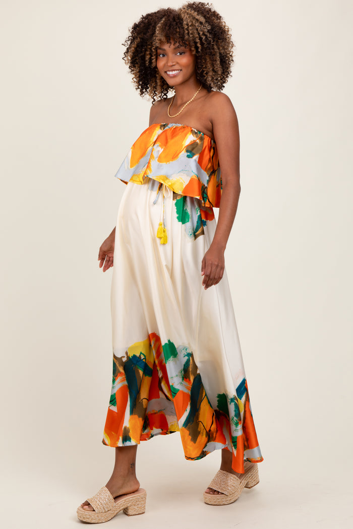 woman wearing a colorful strapless maternity dress with a ruffled overlay and a flowy skirt, showing a baby bump