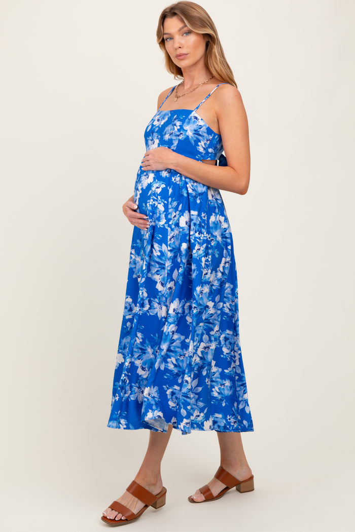 woman wearing a blue floral maternity dress, showcasing her baby bump, with spaghetti straps and a flowing skirt