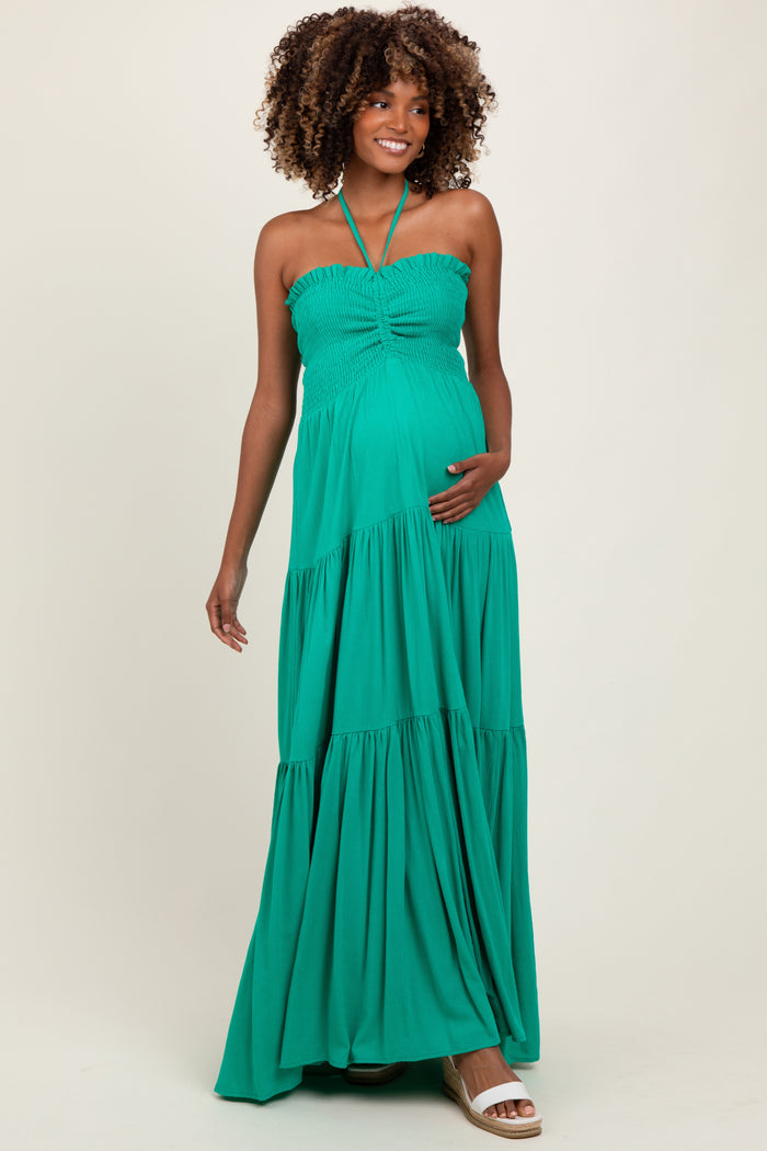 woman wearing a green halter neck maternity maxi dress and holding her baby bump
