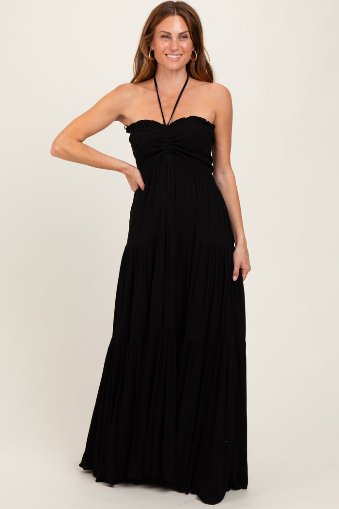 woman wearing a black halter neck maxi dress with a smocked bodice and tiered skirt, smiling and posing with one hand on her hip