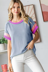 woman wearing a blue ribbed short sleeve top with pink stripes on the sleeves and light colored pants