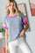 woman wearing a blue ribbed short sleeve top with pink stripes on the sleeves and light colored pants