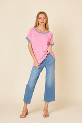 woman wearing a pink ribbed short sleeve top with blue trim and light blue wide leg jeans, standing with one hand on her hip