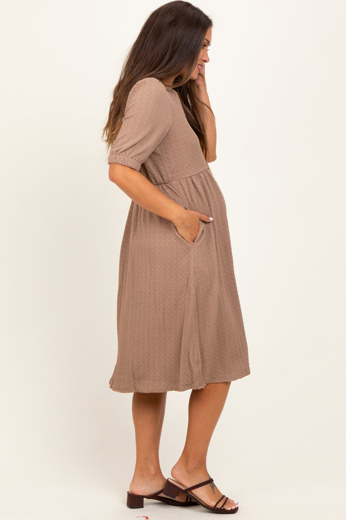 woman wearing a taupe short sleeve maternity dress with a cinched waist and pockets, showing a visible baby bump