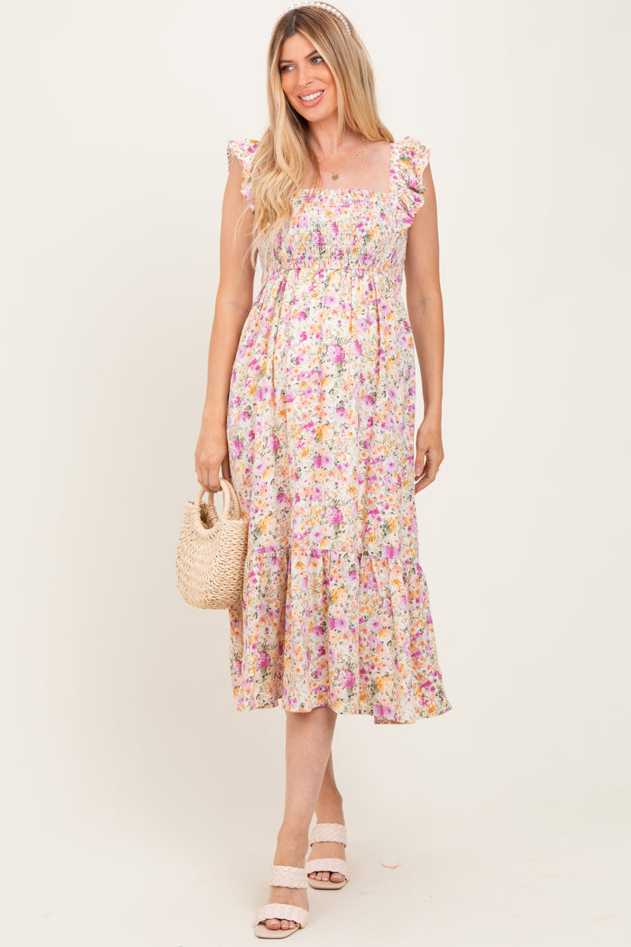 woman wearing a floral maternity maxi dress with ruffled straps and a tiered skirt, holding a woven bag