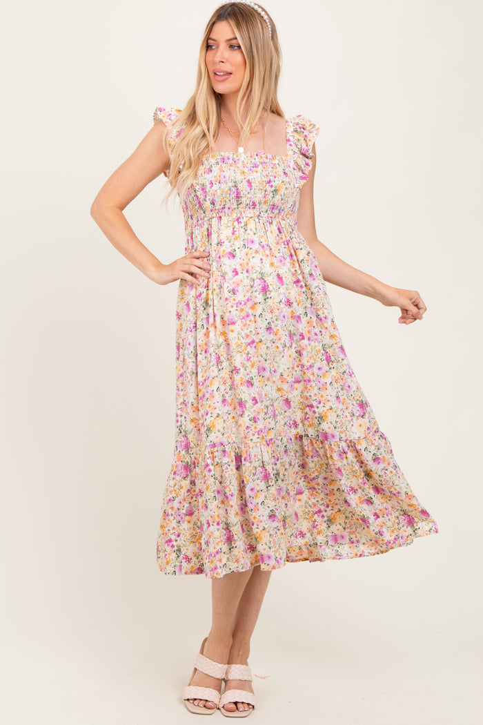 woman wearing a floral print maternity dress with ruffle sleeves and a flowy skirt, standing with one hand on her hip