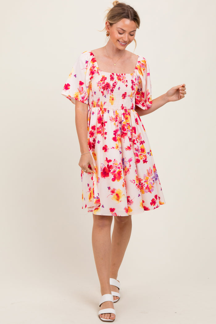 woman wearing a pink floral smocked dress with puff sleeves and a square neckline, smiling and standing in a light pose