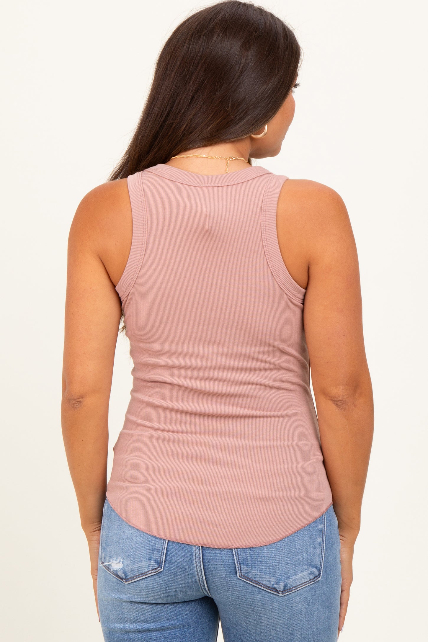 woman wearing a light pink ribbed maternity tank top and blue distressed jeans, showing the back view