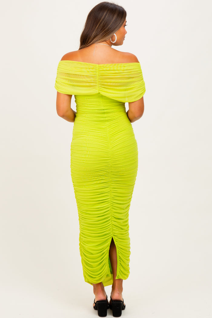 woman wearing a bright green off-the-shoulder maternity dress with ruching details and a back slit