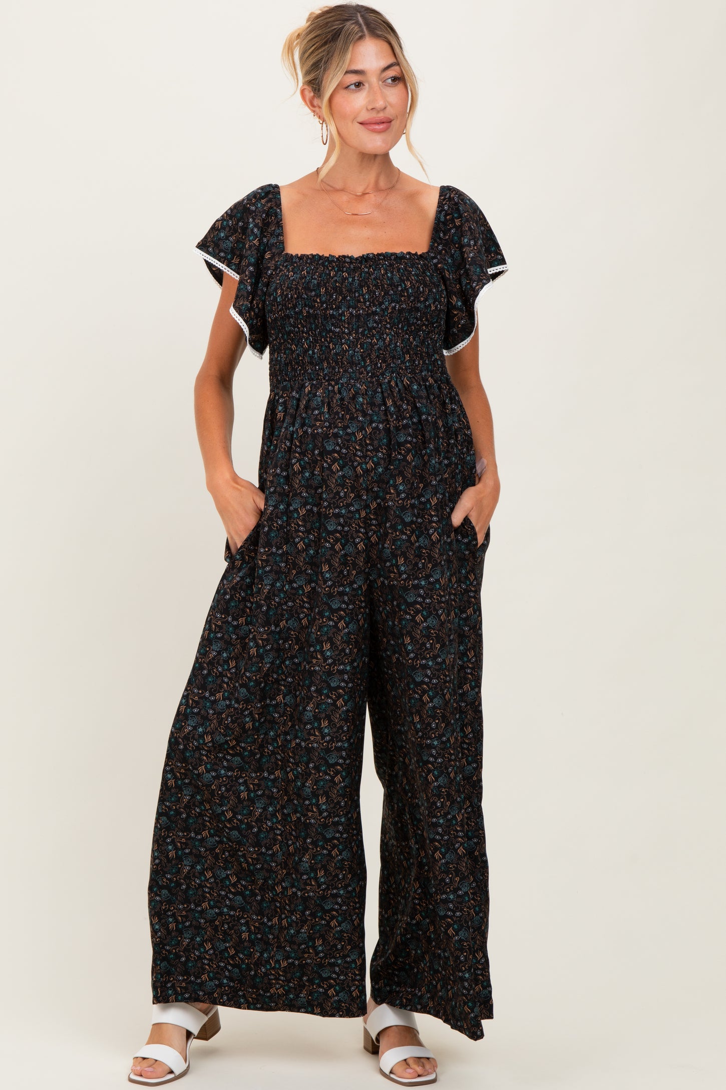 woman wearing a black floral maternity jumpsuit with short ruffled sleeves and pockets, featuring a square neckline