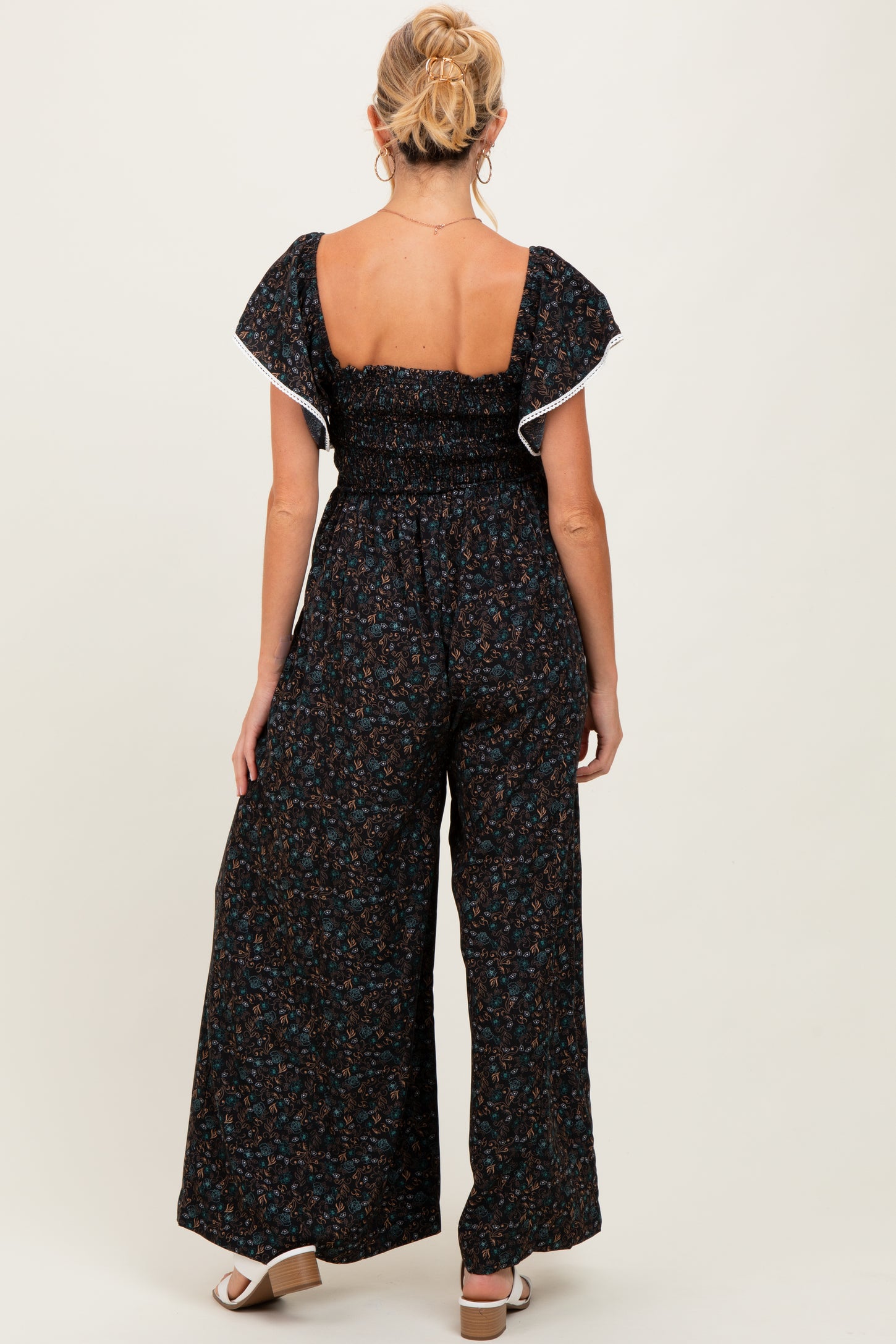 woman wearing a black floral maternity jumpsuit with ruffled sleeves and a smocked back, showing off her baby bump