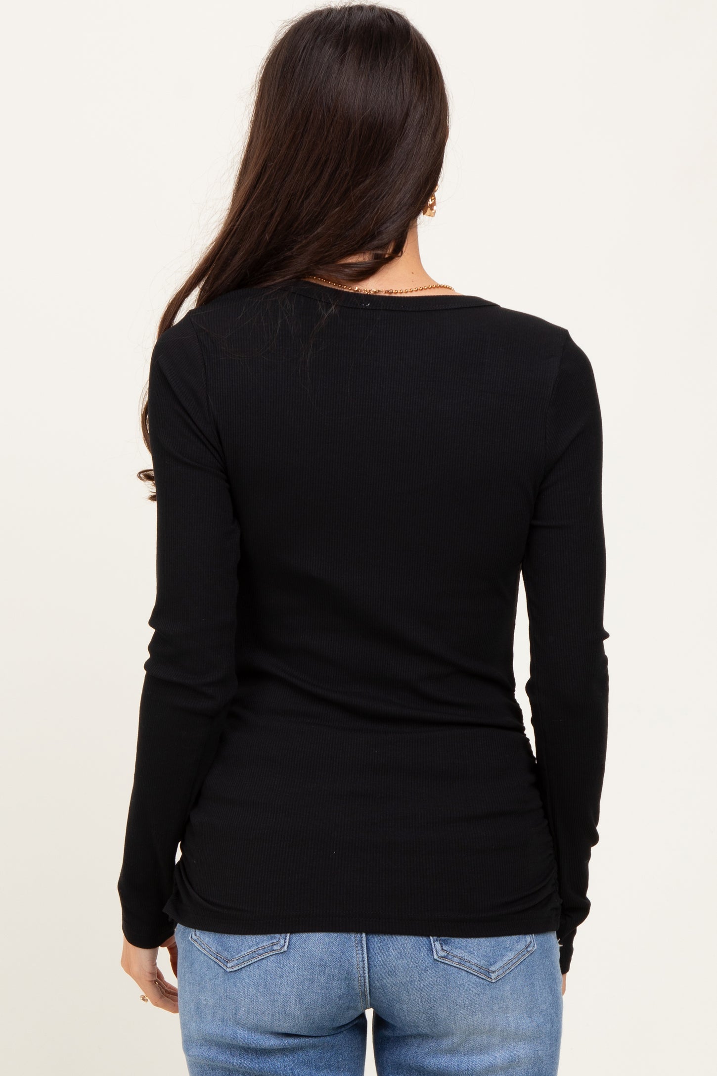 woman wearing a black long sleeve fitted top, seen from the back with her hair down and paired with blue jeans