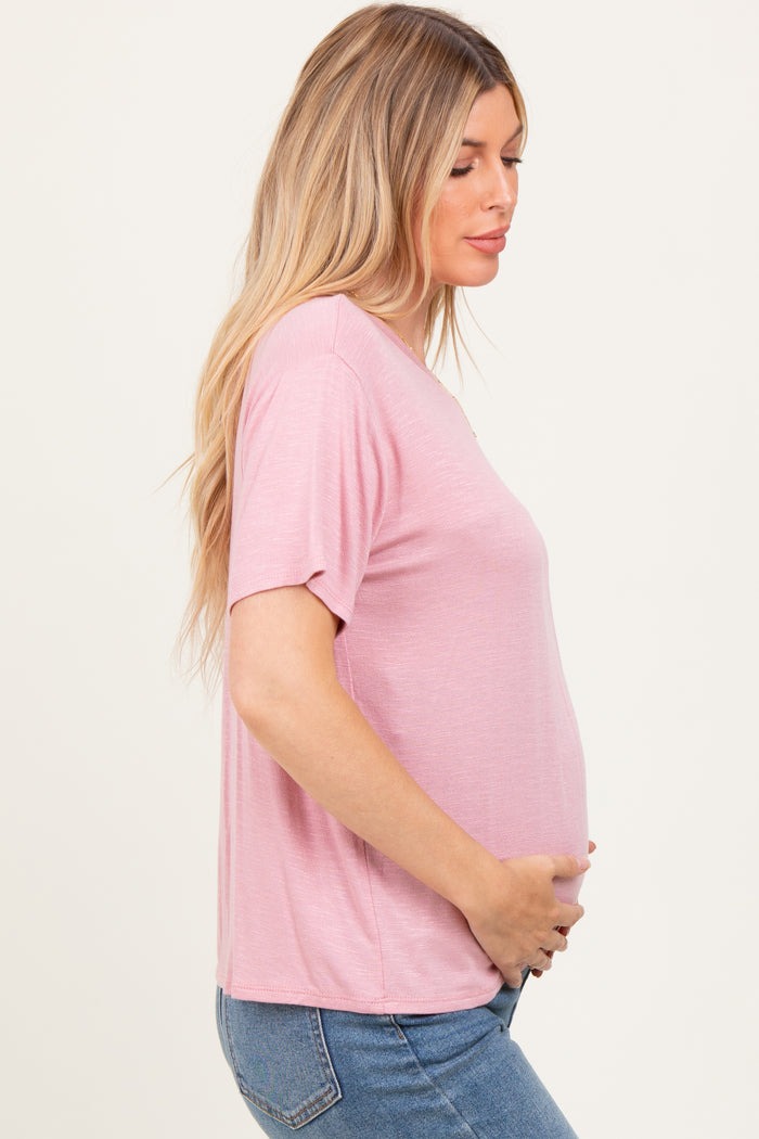 woman wearing a light pink short sleeve maternity top and holding her baby bump