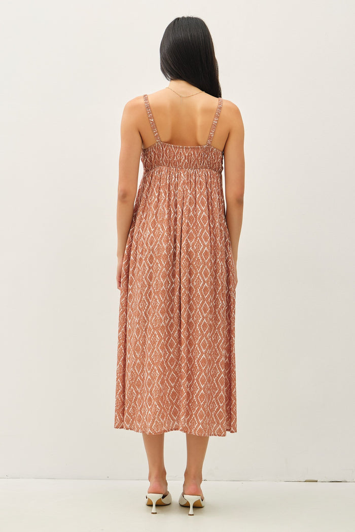 woman wearing a back view of a rust-colored maxi dress with a diamond pattern and adjustable straps