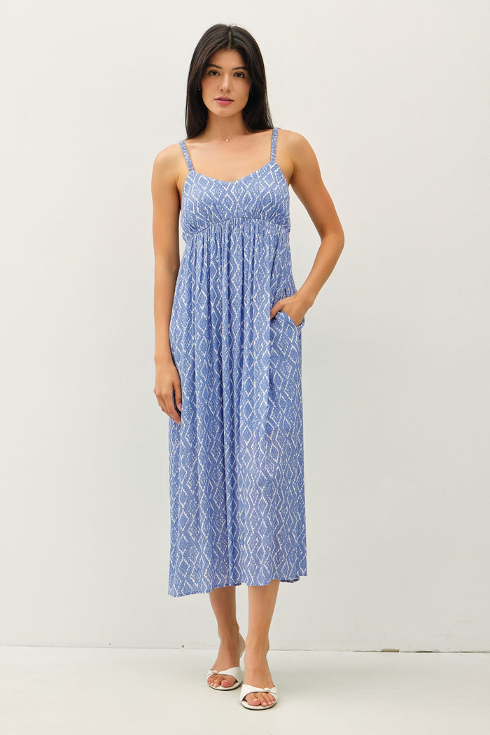 woman wearing a blue patterned sundress with thin straps and pockets, standing against a plain background