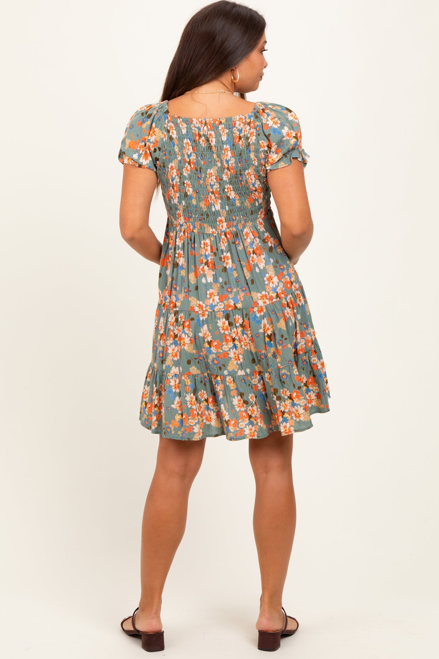 woman wearing a green floral maternity dress with a smocked back and tiered skirt, viewed from the back
