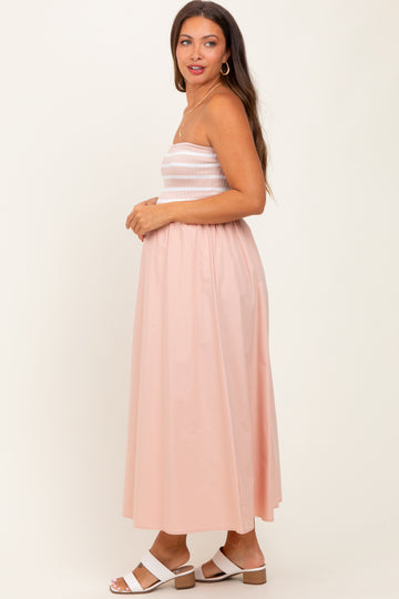 woman wearing a light pink maternity maxi dress with a smocked bodice and a flowing skirt, showing her baby bump