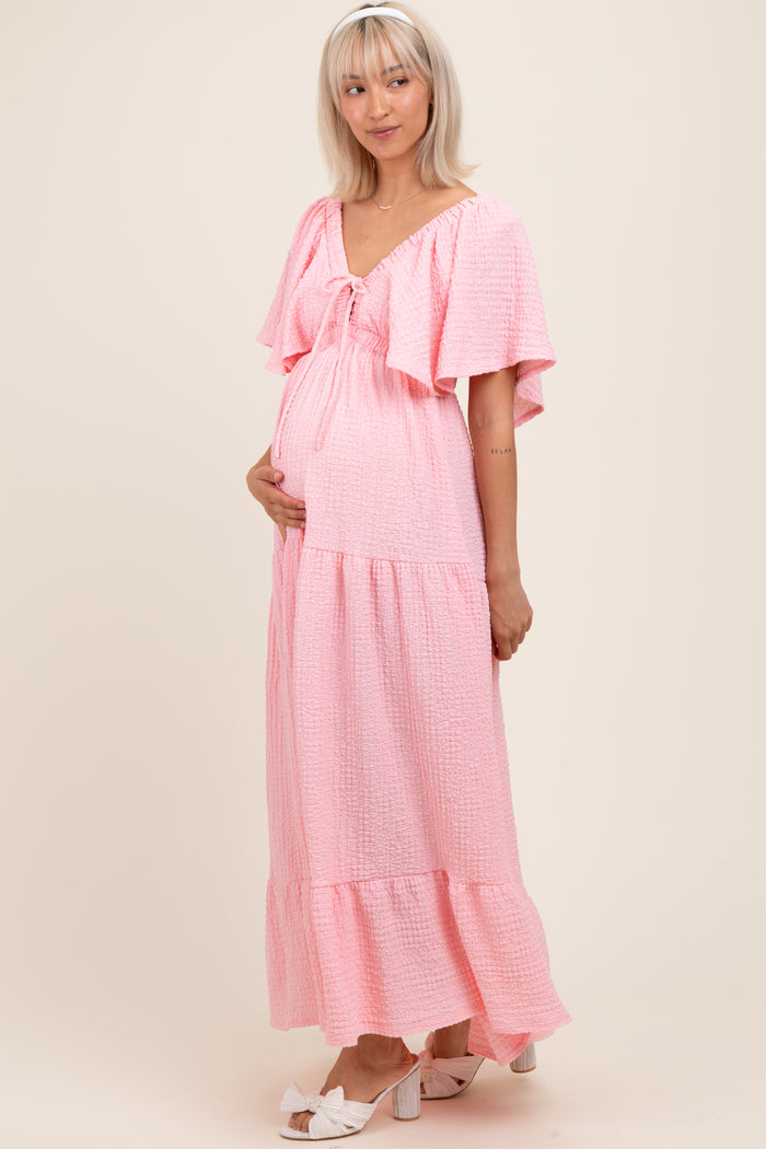 woman wearing a pink maternity maxi dress with frill sleeves and a tiered skirt, highlighting her baby bump