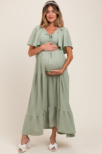woman wearing a green tiered maxi maternity dress and holding her baby bump