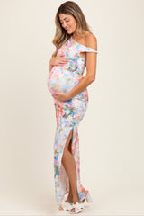 woman wearing a colorful floral off-shoulder maternity gown with a side slit and holding her baby bump