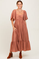 woman wearing a rust-colored maxi dress with puff sleeves and a ruffled hem, posing with hands in pockets