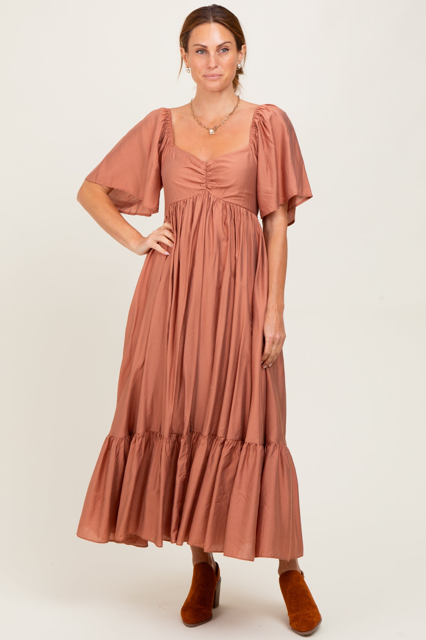 woman wearing a rust colored midi dress with puff sleeves and a tiered skirt, paired with orange ankle boots