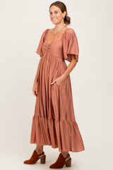 woman wearing a rust-colored maxi dress with puff sleeves and pockets, styled with brown heeled ankle boots