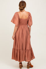 woman wearing a rust-colored maxi dress with short puff sleeves and a smocked back detail