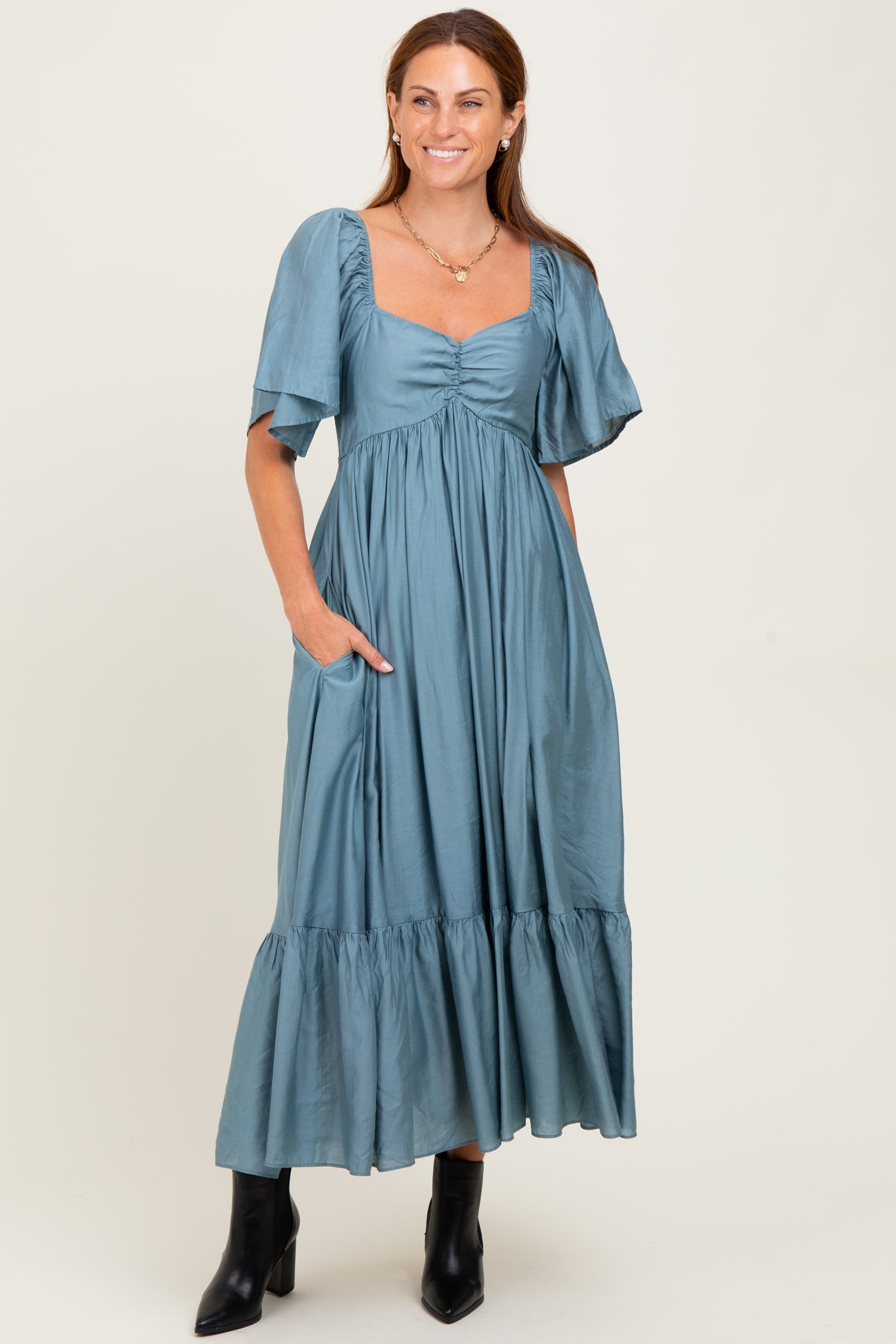 woman wearing a teal maxi dress with short puff sleeves and a tiered skirt, standing with hands in pockets